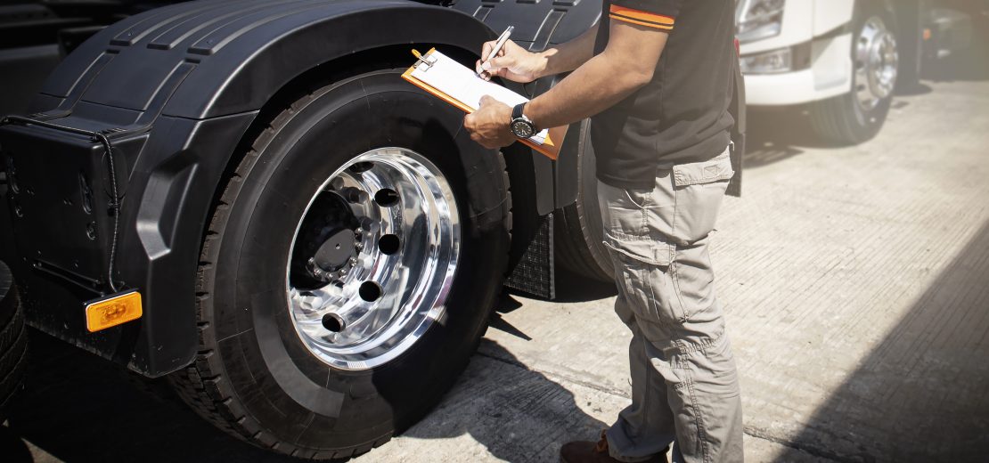 Ein Lkw-Fahrer steht neben seinem Fahrzeug und füllt ein Blatt aus, das auf ein Klemmbrett geklemmt ist.