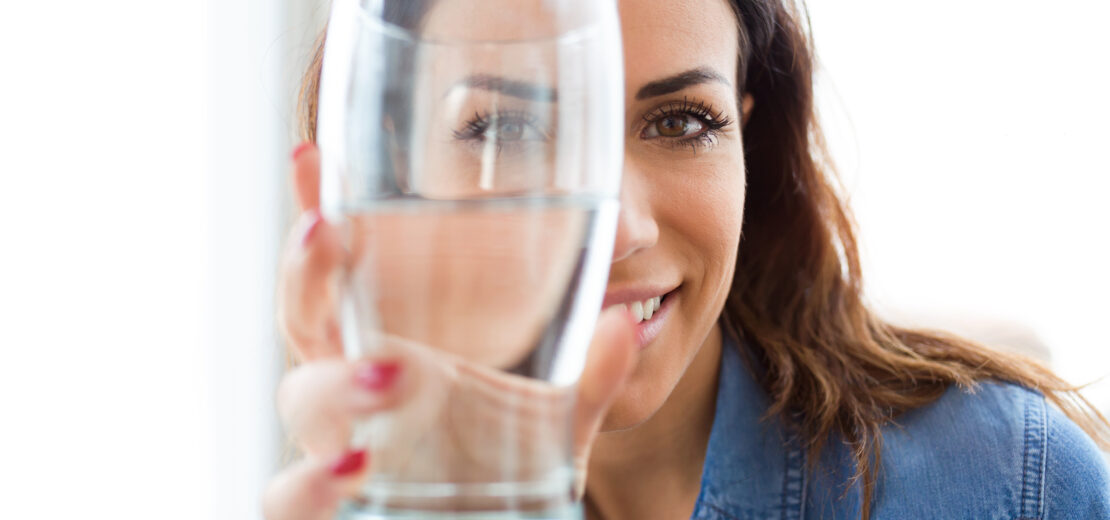 TrinkwaFrau, die ein gefülltes Wasserglas in die Kamera hält.