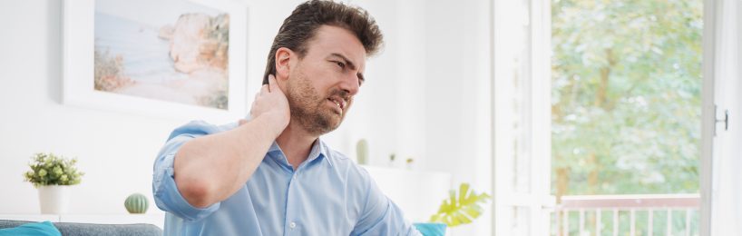 Junger Mann leidet an Nackenschmerzen: Nicht nur im Homeoffice kann fehlende Ergonomie und Bewegung die Gesundheit beeinträchtigen.