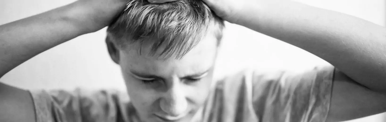 Junger Mann schlägt Hände überm Kopf zusammen. n seinem Gesicht zeichnen sich große psychische Belastungen am Arbeitsplatz ab.