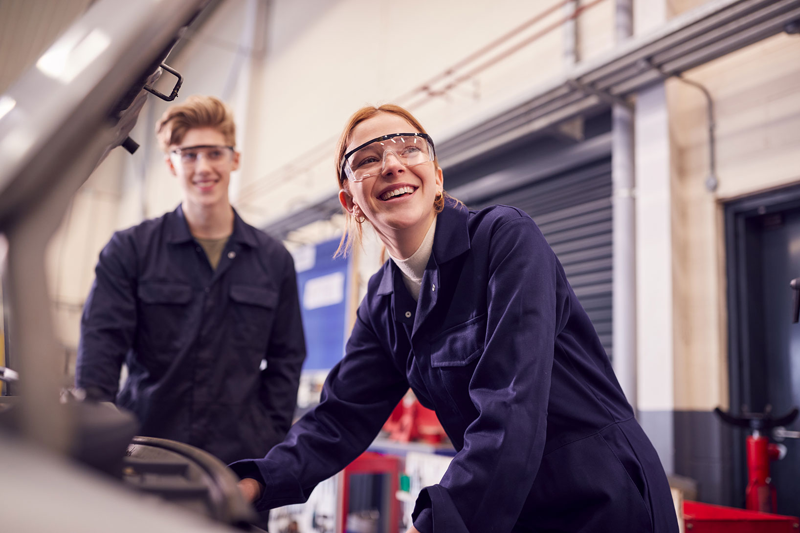 Zwei Praktikanten werden bei ihrem Schülerpraktikum im Rahmen einer Sicherheitsunterweisung in die Gefahren einer Autowerkstatt eingeführt.