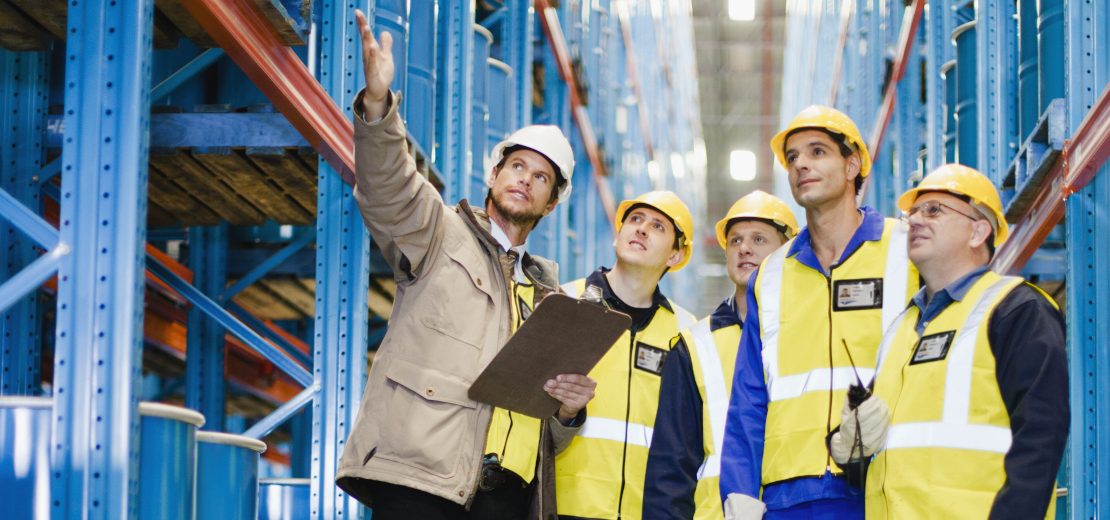 Akteure des betrieblichen Arbeitsschutzes stehen in einer Halle und diskutieren.