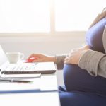 Schwangere Frau haelt sich Bauch und arbeitet
