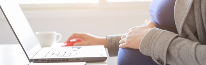 Schwangere Frau haelt sich Bauch und arbeitet
