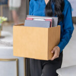 Gekündigte Frau verlässt mit einem gepackten Karton das Büro.