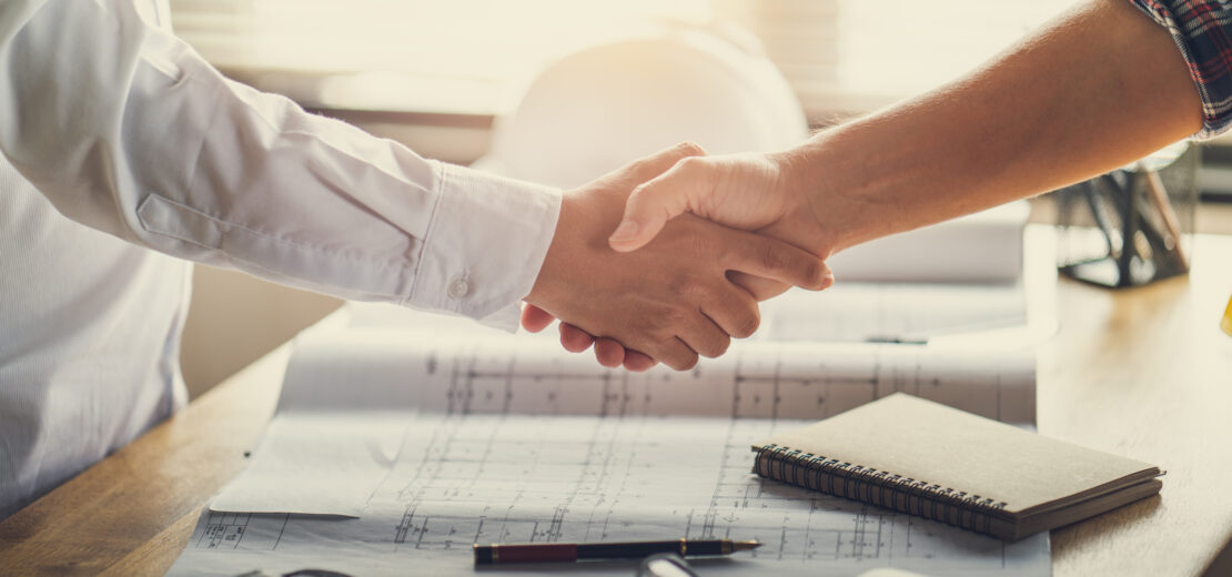 Handschlag über Bauplänen zum erfolgreichen Architektenvertrag