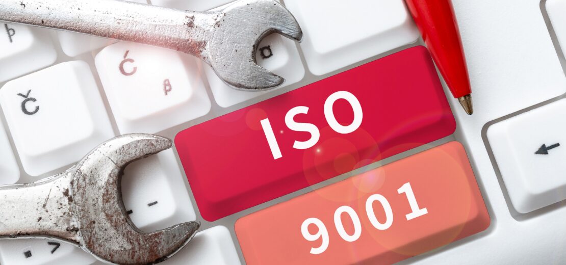 Auf einer PC-Tastatur sind zwei Tasten mit ISO und 9001 beschriftet, daneben liegen zwei unterschiedlich große Schraubenschlüssel