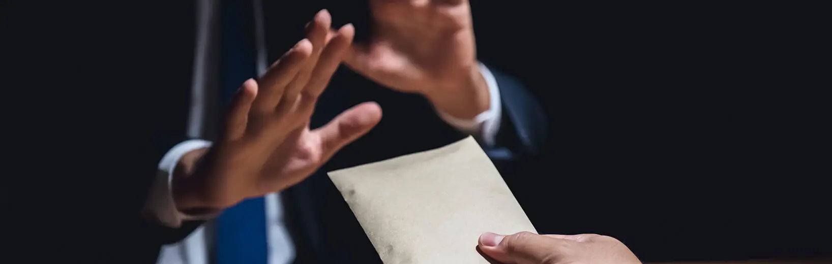 Hinweisgeberschutz: Wie Sie interne Meldestellen einrichten Mann gibt jemandem einen Umschlag, dieser jemand nimmt die Hände in Abwehrhaltung hoch.