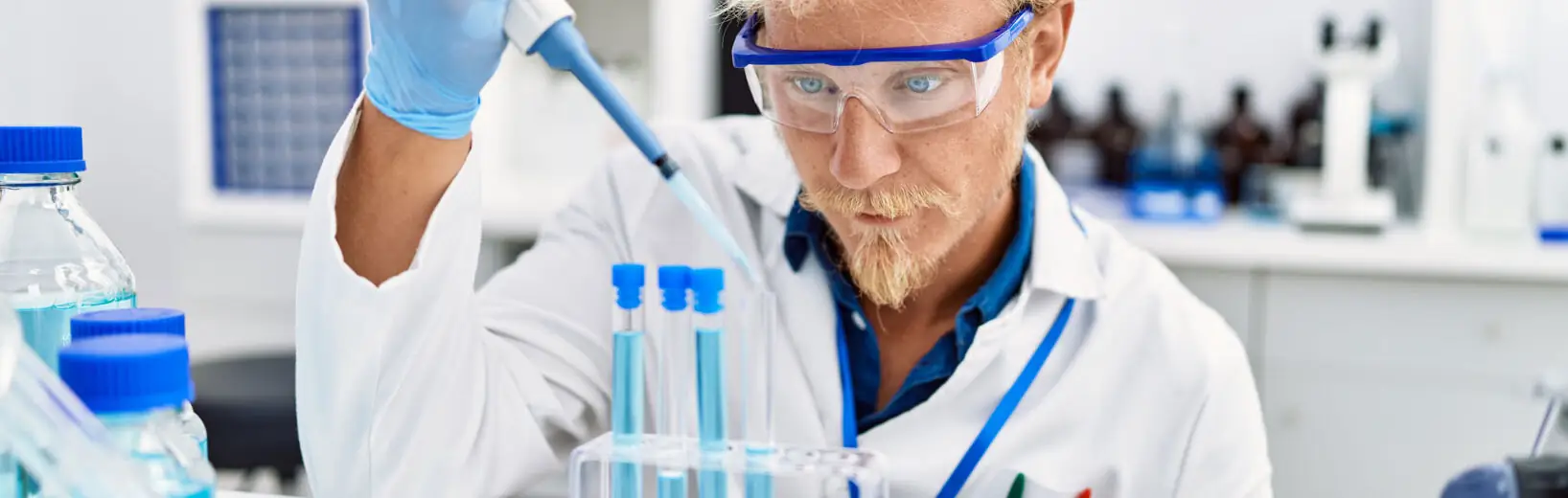 Substitutionsprüfung für Gefahrstoffe Mann in weißem Kittel im Labor betrachtet Reagenzgläschen mit blauer Flüssigkeit: Symbolbild für die Substitutionsprüfung.