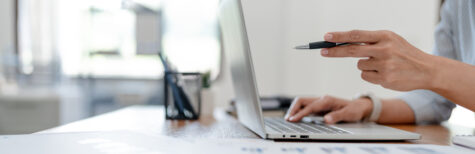 Hand vor Laptop hält Kugelschreiber