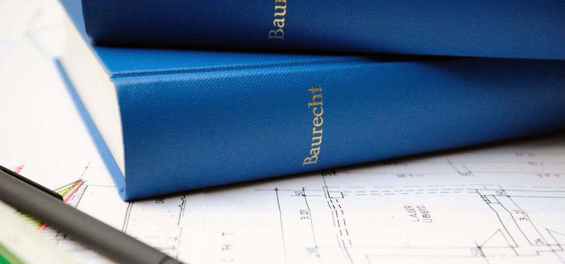 Auf einem Bauplan liegen ein Stift, ein Lineal und zwei Baurecht-Bücher