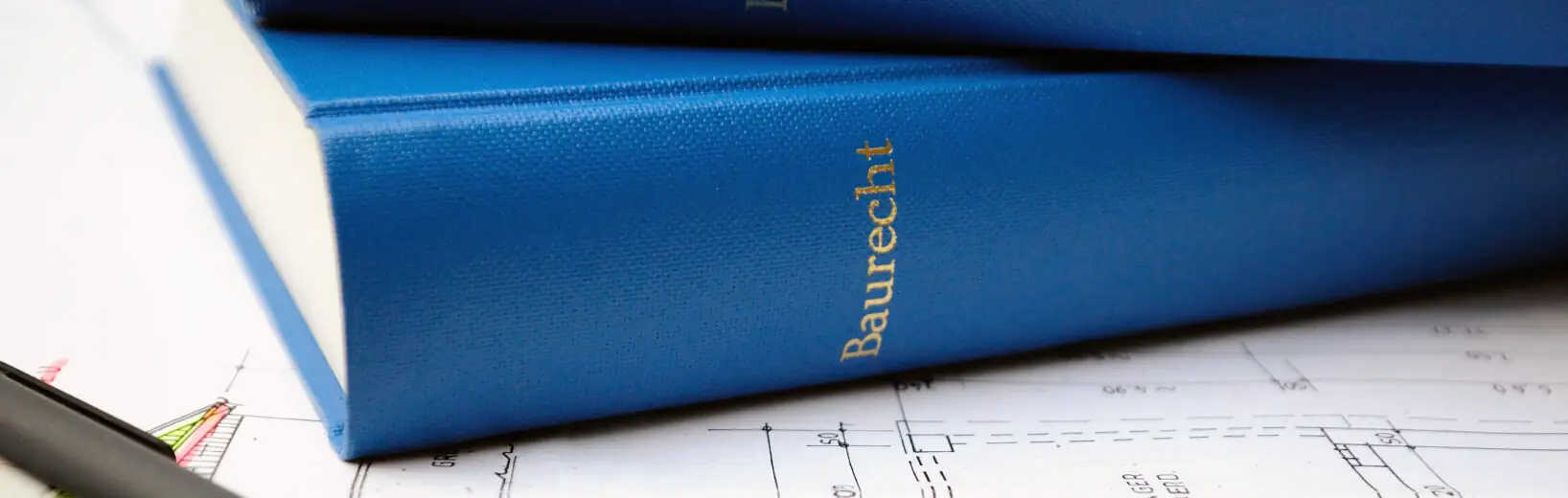BauGB-Novelle 2025: der Status Quo – BauTurbo als erster Schritt bereits in Kraft Auf einem Bauplan liegen ein Stift, ein Lineal und zwei Baurecht-Bücher