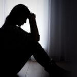 Umriss einer einsamen, traurigen und sitzenden Frau im Schatten