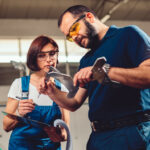 Arbeiterin und Arbeiter an einer CNC Maschine, sie messen das Produkt