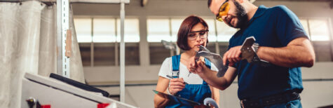 Arbeiterin und Arbeiter an einer CNC Maschine, sie messen das Produkt