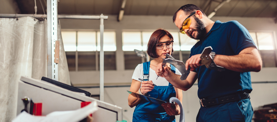 Arbeiterin und Arbeiter an einer CNC Maschine, sie messen das Produkt
