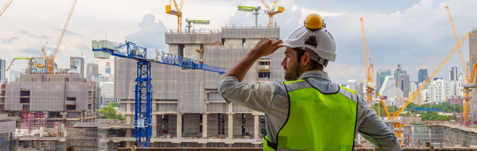 BauTurbo § 246e BauGB in Kraft: Was Planer und Kommunen jetzt wissen müssen Ein Bauarbeiter in einer neongrünen Sicherheitsweste und einem weißen Helm überblickt eine sehr große Baustelle, auf der mehrere Kräne, unfertige Gebäude und die Skyline der Stadt im Hintergrund zu sehen sind. Das Bild vermittelt den Eindruck, dass viele Bauvorhaben gleichzeitig realisiert werden und an jeder Ecke gebaut wird. Dies untermautert den von der Regierung bezeichneteten "BauTurbo §246e", ein Gesetz zur Beschleunigung des Wohnungsbaus und zur Wohnraumsicherung.