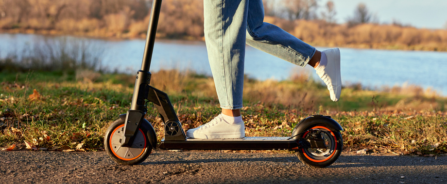Junge Frau fährt mit dem E-Scooter, Nahaufnahme von Bein und Turnschuh