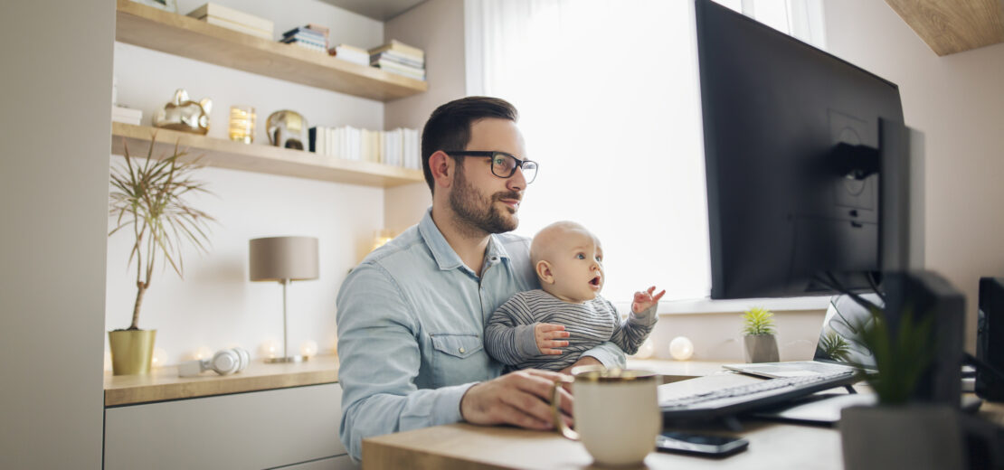Mann sitzt mit Baby vor PC im Homeoffice