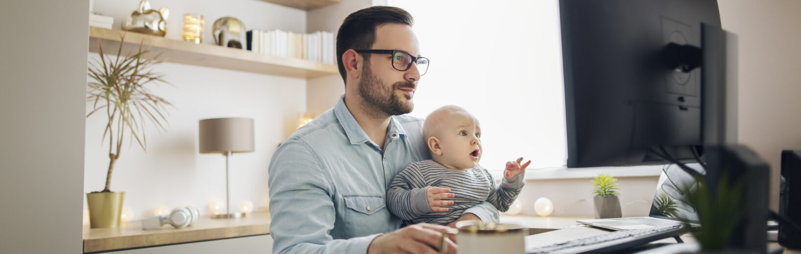 Schlechtere Karrierechancen bei zu viel Homeoffice Mann sitzt mit Baby vor PC im Homeoffice