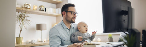 Mann sitzt mit Baby vor PC im Homeoffice