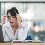 Junge Frau im Büro ist von Hitze schöpft und reibt sich die Stirn