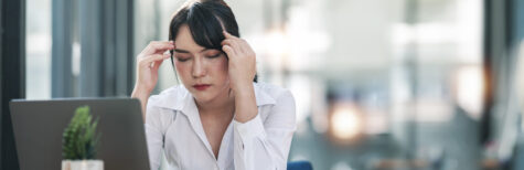 Junge Frau im Büro ist von Hitze schöpft und reibt sich die Stirn