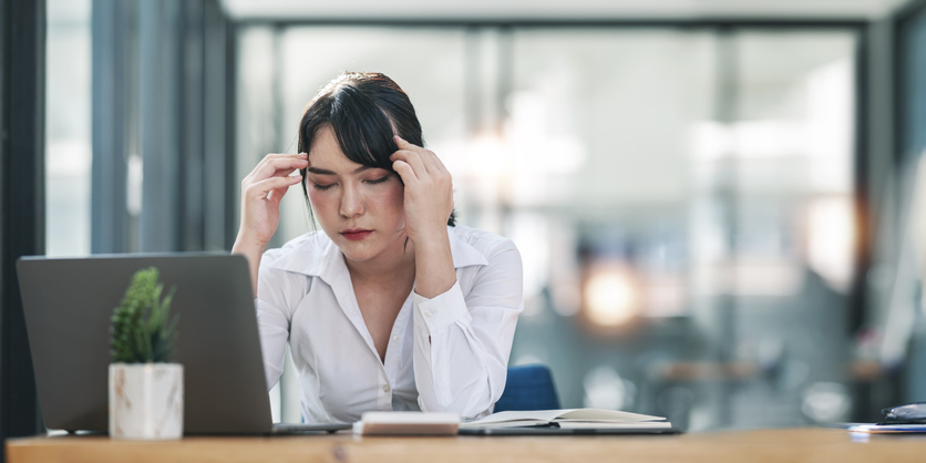 Junge Frau im Büro ist von Hitze schöpft und reibt sich die Stirn