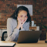 Frau im Homeoffice hat Online-Meeting und sitzt mit Headset vor dem Laptop