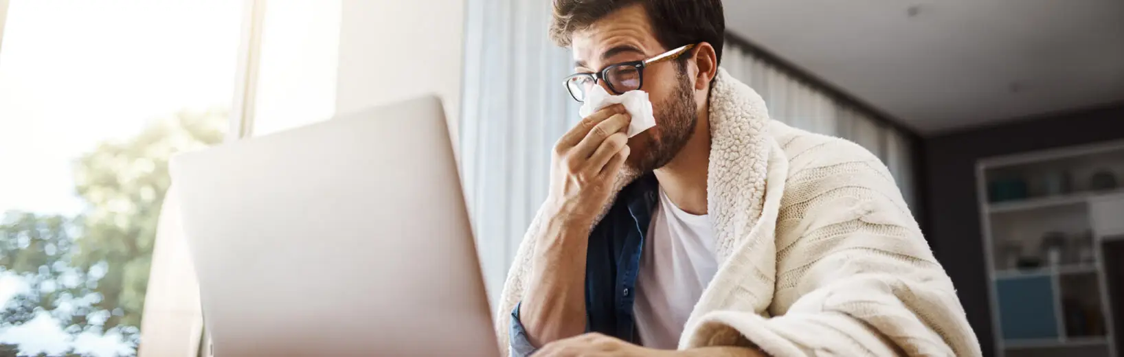 Homeoffice: Arbeiten trotz Krankheit Verschnupfter Mann sitzt am Notebook und arbeitet