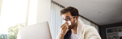 Verschnupfter Mann sitzt am Notebook und arbeitet