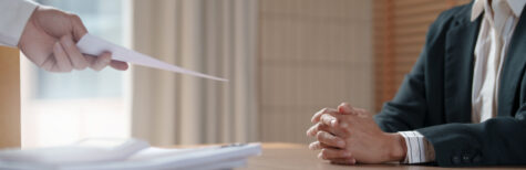Hand reicht sitzenden Mann ein Blatt, eine Kündigung