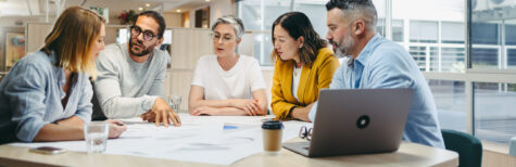 5 Personen sitzen mit einem Notbook um einen Besprechungstisch herum