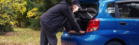 Mann steht im Wald vor seinem Auto und schaut in des geöffneten Kofferraum